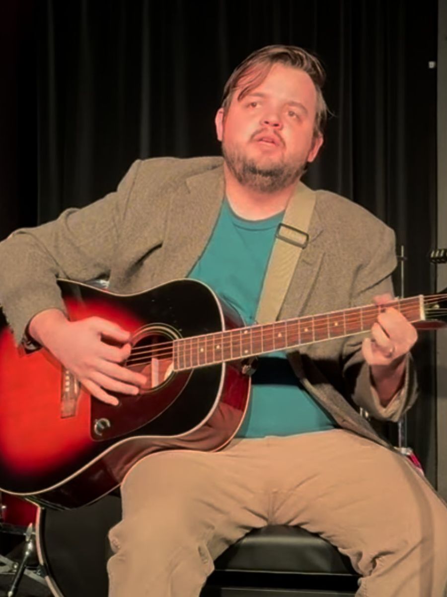 Travis Carroll performing and singing while playing guitar on stage
